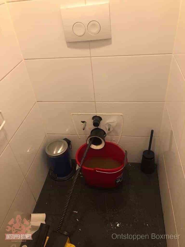 Een ontstopte wand-wc met verwijderde toiletpot waar een ontstoppingsveer in de wanduitgang verdwijnt, het achterhalen waar de verstopping zit in Boxmeer Een ontstopte wand-wc met verwijderde toiletpot waar een ontstoppingsveer in de wanduitgang verdwijnt, het achterhalen waar de verstopping zit in Boxmeer