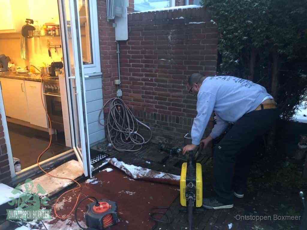 Een monteur werkt buiten bij een open riool-/grondput met een elektrische ontstoppingsmachine om een verborgen afvoerprobleem op te sporen in Boxmeer