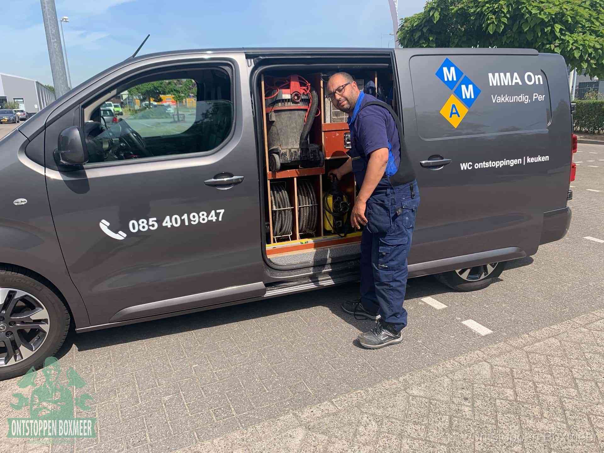 Een monteur bij de open schuifdeur van zijn bedrijfsbus op een parkeerplaats, klaar om de oorzaak van terugkerende afvoerverstoppingen aan te pakken in Boxmeer