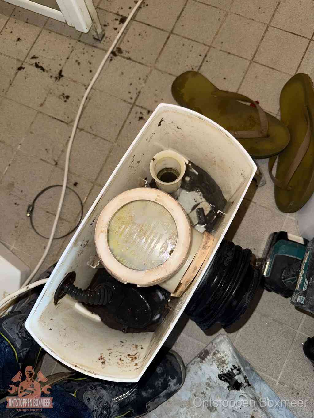 Een gedemonteerde toiletpot op de vloer met ontstoppingsveer en gereedschap ernaast, het verwijderen van een vastzittend voorwerp uit de wc in Boxmeer Een gedemonteerde toiletpot op de vloer met ontstoppingsveer en gereedschap ernaast, het verwijderen van een vastzittend voorwerp uit de wc in Boxmeer