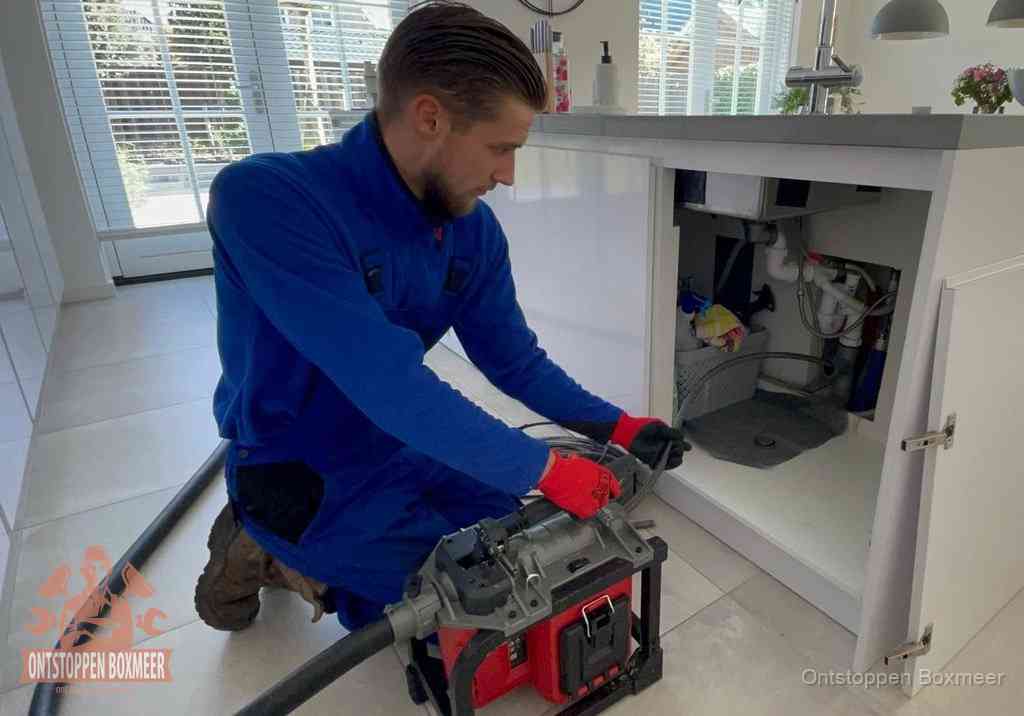 Een monteur voert een professionele elektrische ontstoppingsmachine in de afvoer onder de spoelbak tijdens het gootsteen ontstoppen in Boxmeer Een monteur voert een professionele elektrische ontstoppingsmachine in de afvoer onder de spoelbak tijdens het gootsteen ontstoppen in Boxmeer