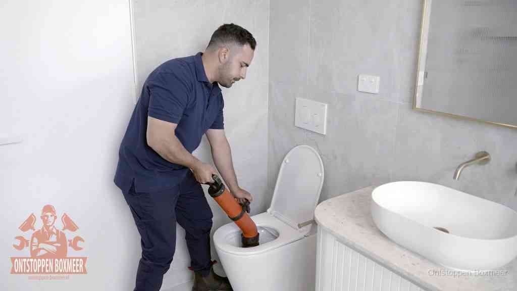 Een man gebruikt een handmatige luchtdruk-ontstopper in een modern betegeld toilet om zelf de wc te ontstoppen in Boxmeer Een man gebruikt een handmatige luchtdruk-ontstopper in een modern betegeld toilet om zelf de wc te ontstoppen in Boxmeer